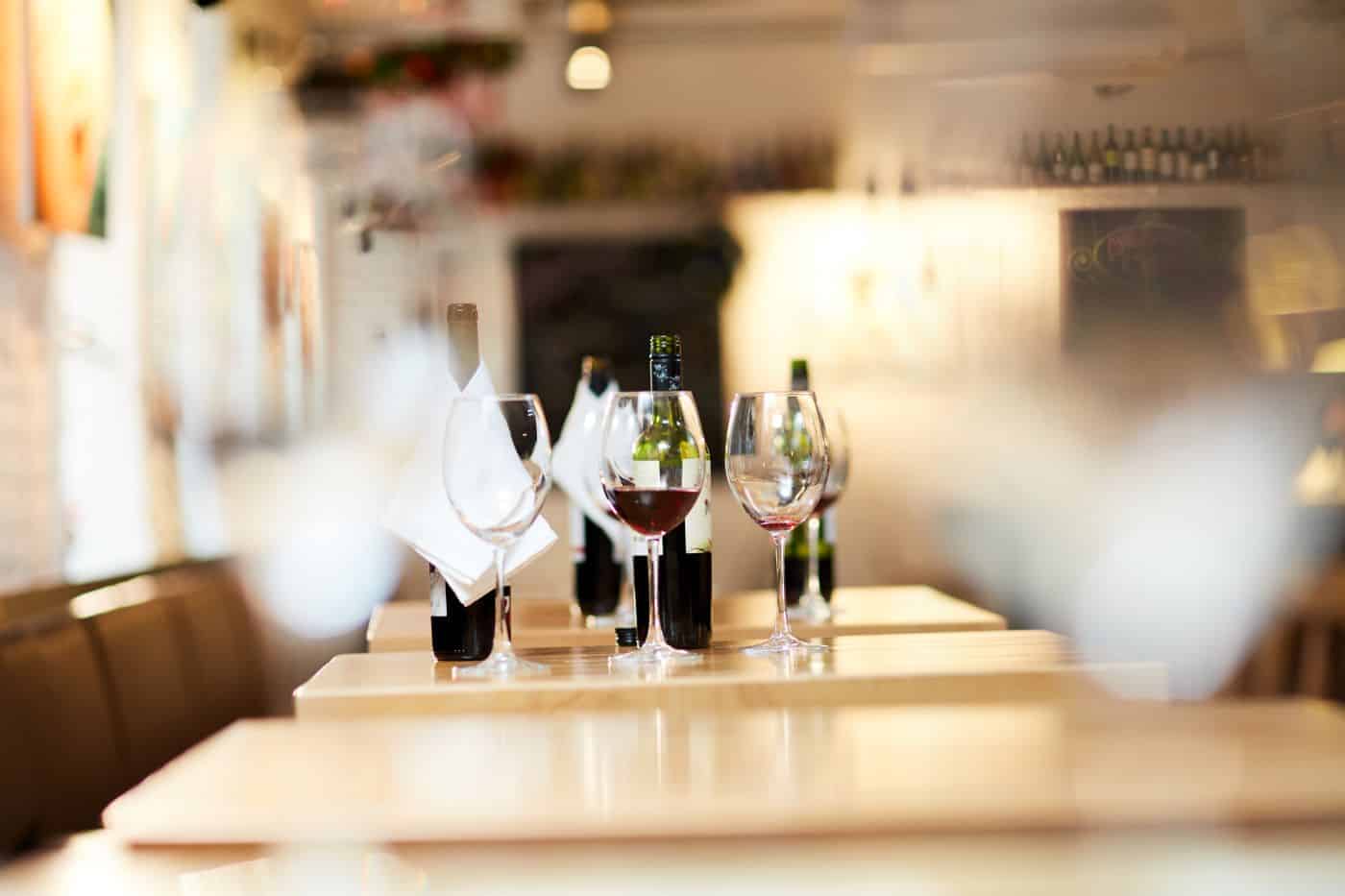 A restaurant table set with wine bottles, wine glasses, and napkins on a blurred background.